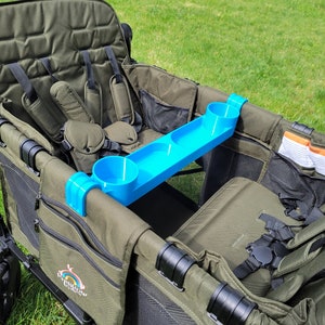 May include: A green wagon with two seats and a blue cup holder tray. The wagon has a black frame and black straps. The wagon has a black mesh pocket on the side and a logo that says "Rainbow Wagon".