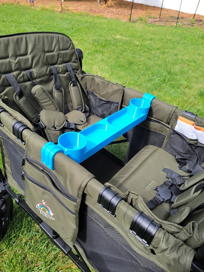 May include: A green wagon with two seats and a blue cup holder tray. The wagon has a black frame and black straps. The wagon has a black mesh pocket on the side and a logo that says "Rainbow Wagon".