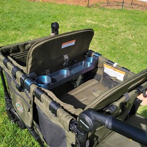 May include: A green folding wagon with a black frame and a black handle. The wagon has a black mesh storage area and a black cup holder. The wagon is open and the lid is up.