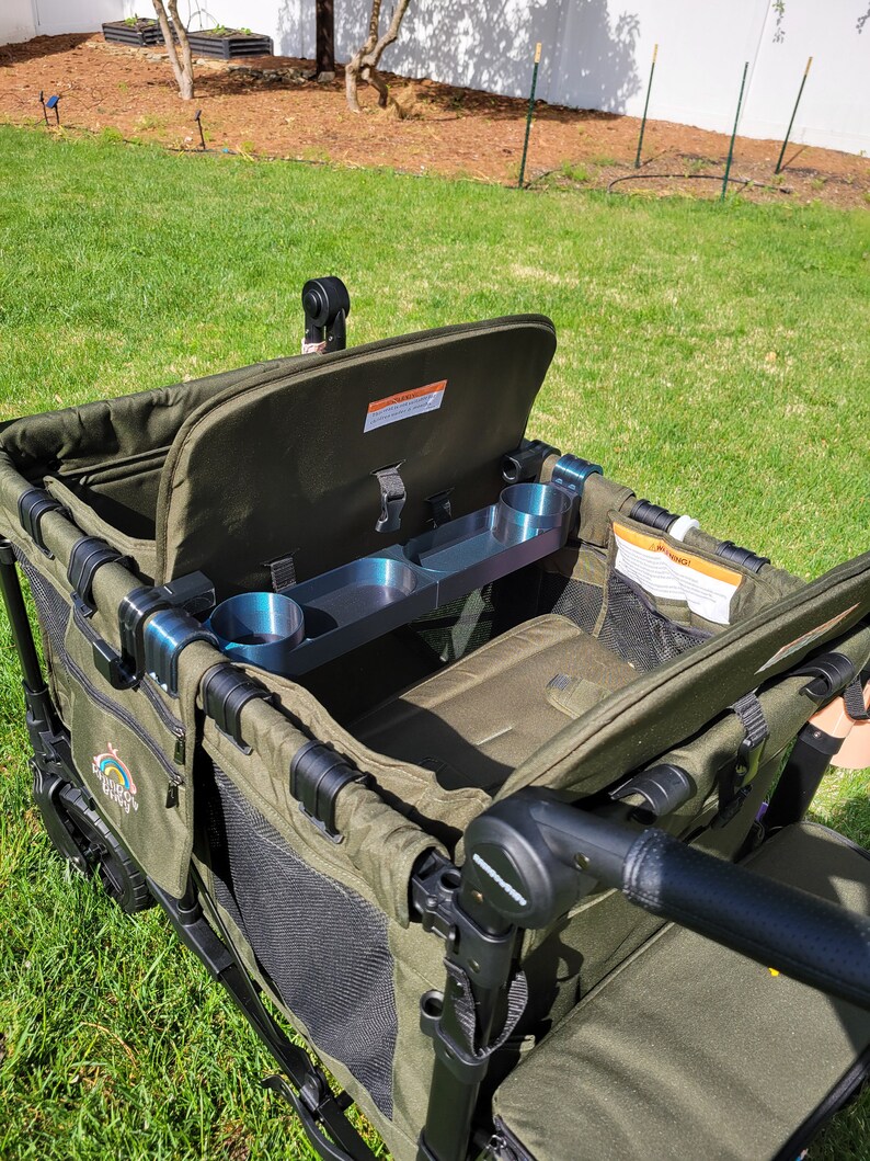 May include: A green folding wagon with a black frame and a black handle. The wagon has a black mesh storage area and a black cup holder. The wagon is open and the lid is up.