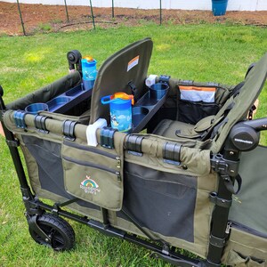 May include: A green and black wagon with two seats, cup holders, and a storage compartment. The wagon has a black handle and a black frame. The wagon is on a grassy lawn. The wagon has a logo that says "Rainbow Bridge".