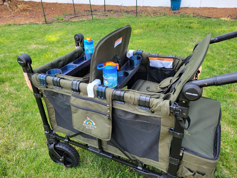 May include: A green and black wagon with two seats, cup holders, and a storage compartment. The wagon has a black handle and a black frame. The wagon is on a grassy lawn. The wagon has a logo that says "Rainbow Bridge".
