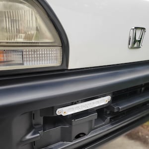 May include: White Honda van with a black bumper and a white license plate frame with the word "SPRINTER" on it.