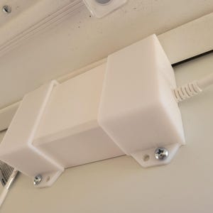 May include: White plastic box with a cord attached to it. The box is mounted to a white surface with screws.