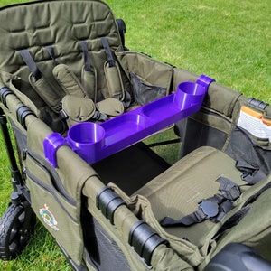May include: A purple cup holder accessory for a wagon or stroller. The cup holder has three slots for cups or bottles and is attached to the side of the wagon.