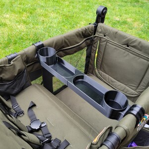 May include: A black plastic cup holder with two cup holders and a tray. The cup holder is attached to the side of a green wagon.