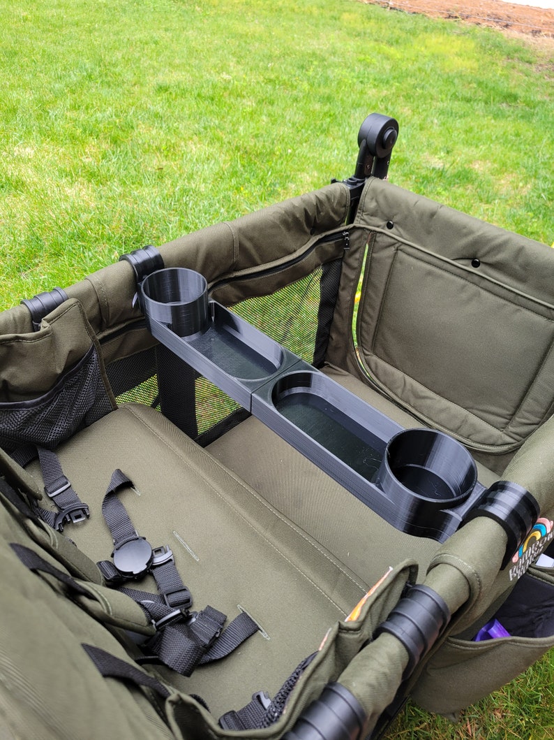 May include: A black plastic cup holder with two cup holders and a tray. The cup holder is attached to the side of a green wagon.