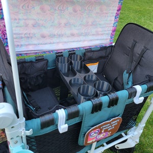 May include: A teal and white wagon with a black and gray cup holder. The wagon has a black mesh storage area and a black fabric seat. The wagon has a pink and white canopy with an octopus pattern. The wagon has a white hook on the side and a brown patch with the text "every adventure begins with a ride".