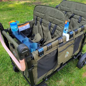 May include: A green wagon with two seats, black mesh sides, and a black frame. The wagon has two cup holders and a storage pocket. The wagon is on a grassy lawn.