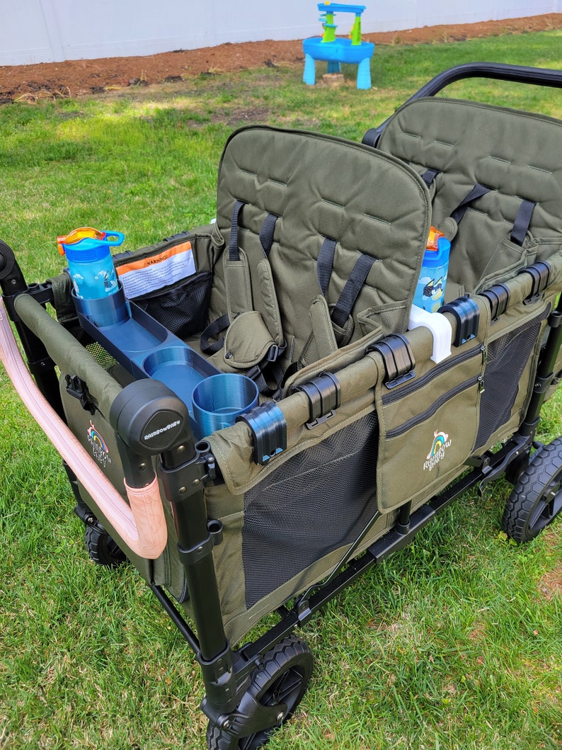 May include: A green wagon with two seats, black mesh sides, and a black frame. The wagon has two cup holders and a storage pocket. The wagon is on a grassy lawn.