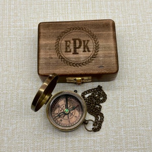May include: A wooden box with a compass inside. The box is engraved with the initials "EPK" in a laurel wreath. The compass is brass with a green jewel in the center.