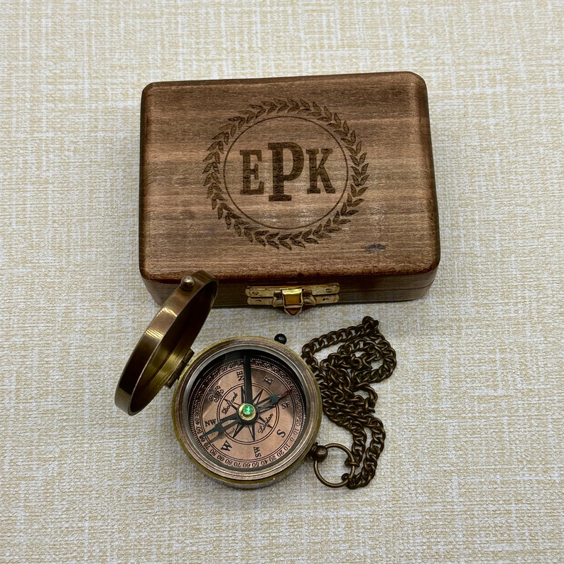 May include: A wooden box with a compass inside. The box is engraved with the initials "EPK" in a laurel wreath. The compass is brass with a green jewel in the center.