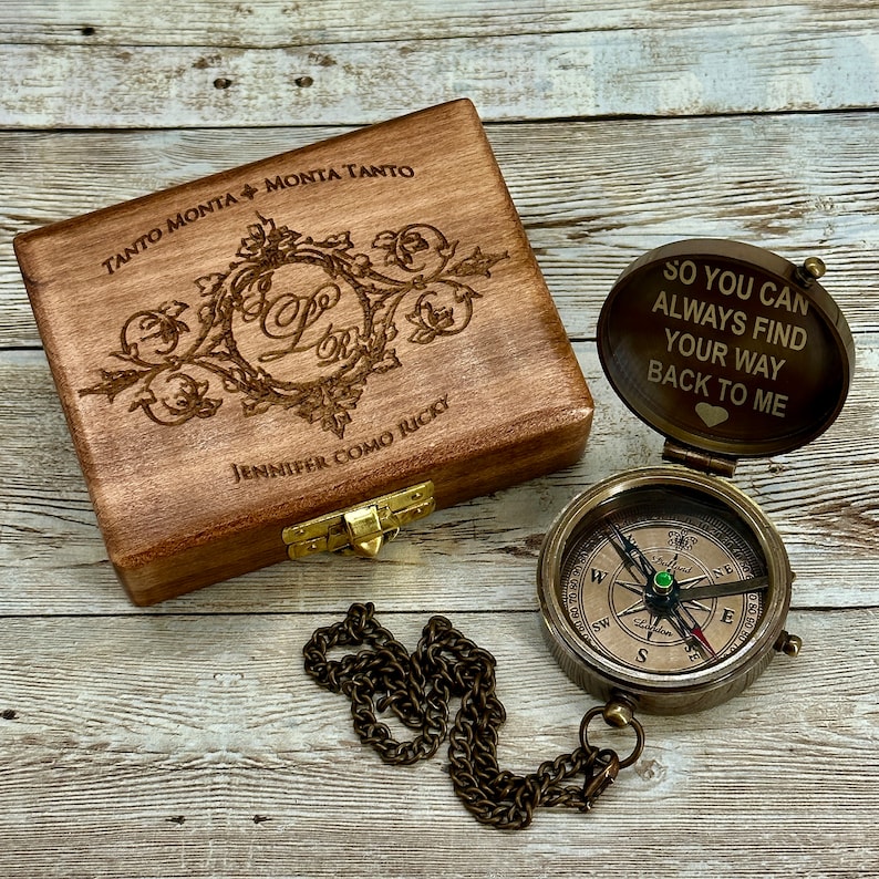 May include: A wooden box with an engraved design and the text "TANTO MONTA MONTA TANTO" and "JENNIFER COMO RICKY". A compass with a chain is attached to the box. The compass has a glass lid with the text "SO YOU CAN ALWAYS FIND YOUR WAY BACK TO ME" engraved on it.