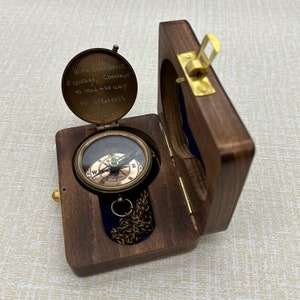 May include: A wooden box with a hinged lid, containing a brass compass with a green jewel. The compass has a chain attached to it. The lid of the box has an inscription that reads: "With confidence & courage, continue to lead the way to greatness."