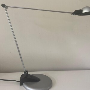 May include: A silver desk lamp with a black shade and a round base. The lamp is adjustable and has a long arm.