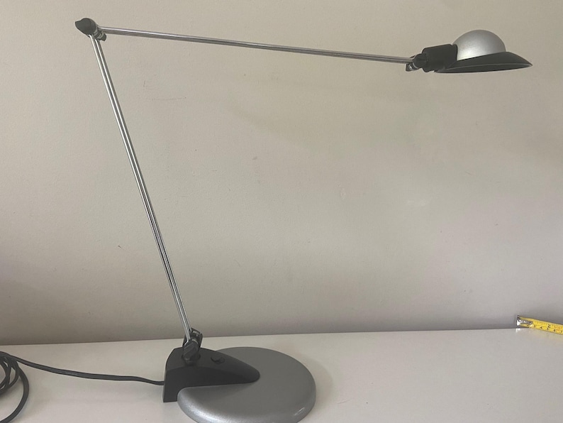 May include: A silver desk lamp with a black shade and a round base. The lamp is adjustable and has a long arm.