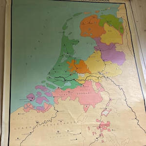 May include: A vintage wall map titled DE REPUBLIEK DER VII VERENIGDE NEDERLANDEN, featuring a colorful historical depiction of the Netherlands and surrounding regions with distinct green, orange, yellow, and pink territories on a cream background.