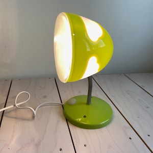 May include: A green desk lamp with a white cord and a white light bulb. The lampshade has a heart-shaped cutout design.