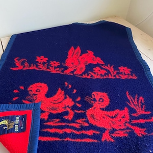 May include: A navy blue blanket with a red design featuring a rabbit, ducks, and flowers. The blanket has a red interior and a blue border. The words "GOOD NIGHT" are visible on a tag.
