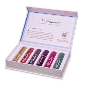 May include: A white box with a blue lid containing six small glass bottles with colorful liquids. The bottles are labeled "Sensametrix" and are part of a smell identification and training kit. The lid has instructions on how to use the kit and a QR code to scan for more information.