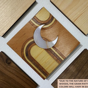 May include: Wooden wall art featuring a central square with a crescent moon and retro-style arch design. Surrounding squares showcase various wood grains and colors. The text at the bottom states, "DUE TO THE NATURE OF REAL WOODS, THE GRAIN PATTERNS & COLORS WILL VARY IN EACH PIECE."