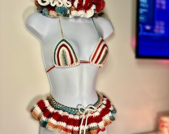 May include: A crocheted bikini set with a matching hat. The bikini top and bottom are striped in red, white, brown, and teal. The hat is white with red, brown, and teal stripes and has a ruffled edge.