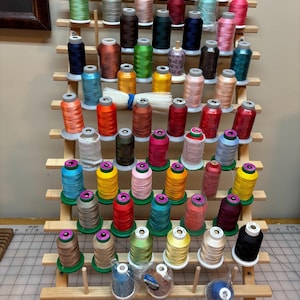 以下が含まれることがあります： カラフルな刺繍糸の糸巻きが複数ある木製糸立て。糸立ては7段あり、「June Tailor」とラベルが貼られています。