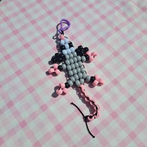 May include: A gray, pink, and black beaded animal keychain with a purple loop. The animal is a rat or mouse with a long tail.