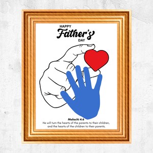 May include: A framed print with a gold-colored wooden frame. The print features a black and white illustration of hands holding a red heart and a blue handprint. Text reads "Happy Father's Day" and a Bible verse.