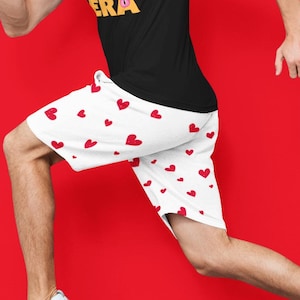 May include: A black short-sleeved t-shirt with the yellow text IN MY DUNGEON CRAWLING ERA and a small pink icon, paired with white athletic shorts featuring a repeating pattern of small red hearts and white sneakers with blue stripes.