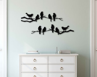 May include: Black metal wall decor featuring a silhouette of birds perched on branches. The decor is mounted on a white wall above a white dresser with six drawers.