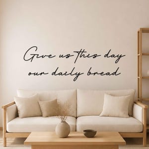 Op de afbeelding: Een zwart wandbord met de cursieve tekst Give us this day our daily bread. De belettering is gerangschikt in twee regels, waarbij de eerste regel Give us this day leest en de tweede regel our daily bread leest, gemonteerd op een muur.