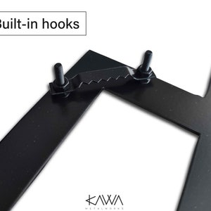 May include: Close-up of a black metal letter with built-in hooks. The hooks are made of metal and have a serrated edge. The letter is part of a metal letter set.
