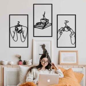 May include: Three black and white line art prints of people holding coffee mugs. The prints are framed and hung on a white wall.