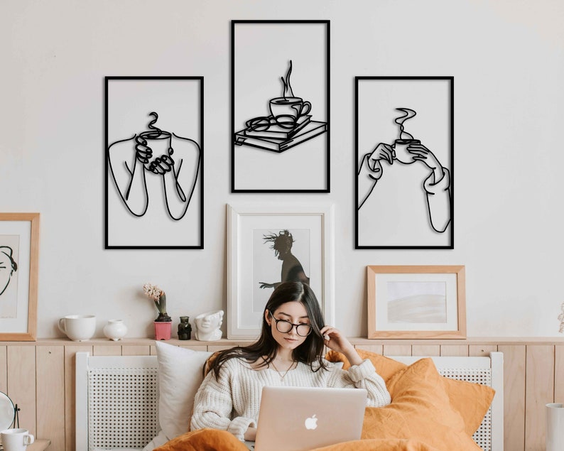 May include: Three black and white line art prints of people holding coffee mugs. The prints are framed and hung on a white wall.