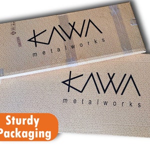May include: Two brown cardboard boxes with the text "KAWA metalworks" printed on them. The boxes are stacked on top of each other. The text "Sturdy Packaging" is printed in orange on a white background.