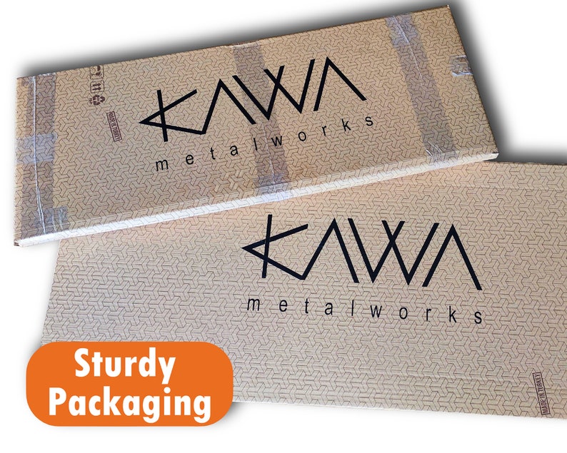 May include: Two brown cardboard boxes with the text "KAWA metalworks" printed on them. The boxes are stacked on top of each other. The text "Sturdy Packaging" is printed in orange on a white background.