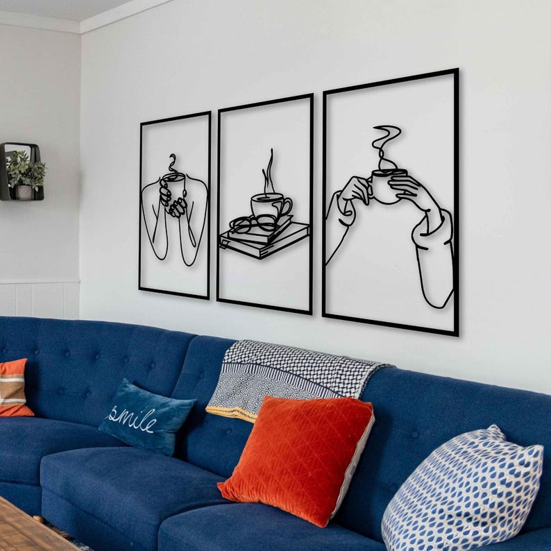 May include: Three black metal wall art pieces featuring a minimalist line art design of a person holding a cup of coffee. The art pieces are framed in black and hung on a white wall above a blue sofa.