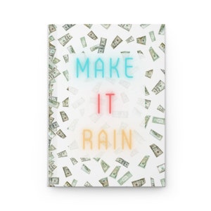 Peut inclure: Un carnet blanc avec un motif d'argent qui tombe et les mots "MAKE IT RAIN" en lettrage de style néon. Le texte est en bleu, rouge et jaune. Le carnet est entouré d'images de billets de banque américains.