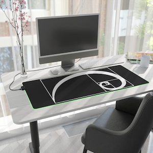 May include: Black rectangular desk mat featuring a white Fibonacci spiral design and a green illuminated edge. The mat is on a white desk with a computer, keyboard, and mouse. A black chair is in the foreground.
