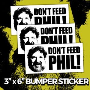 May include: Three white bumper stickers with the text "DON'T FEED PHIL!" in bold black letters. Each sticker features a black and white image of a man's face. The stickers are approximately 7.6 cm x 15.2 cm in size.