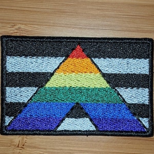 May include: A black and white striped patch with a rainbow colored triangle in the center. The triangle is a pyramid shape with the colors red, orange, yellow, green, blue, indigo, and violet.