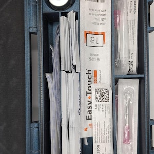 May include: A blue medical case with various medical supplies. The case contains a vial, syringes, needles, and packaging labeled "Easy Touch" and "McKesson Needle". The syringes are 1 cc in size.