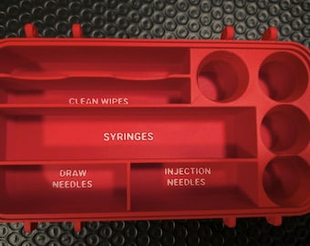 May include: A red organizer with compartments labeled for medical supplies. The organizer has sections for clean wipes, syringes, draw needles, and injection needles. It also has several circular compartments.