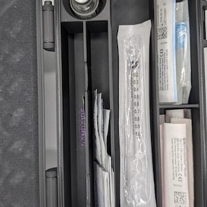 May include: A black, compartmentalized case containing medical supplies. The case holds a vial, syringes, needles, and BAND-AIDS. The case is designed to organize and store medical items. The case is made of a durable material and has a secure closure.