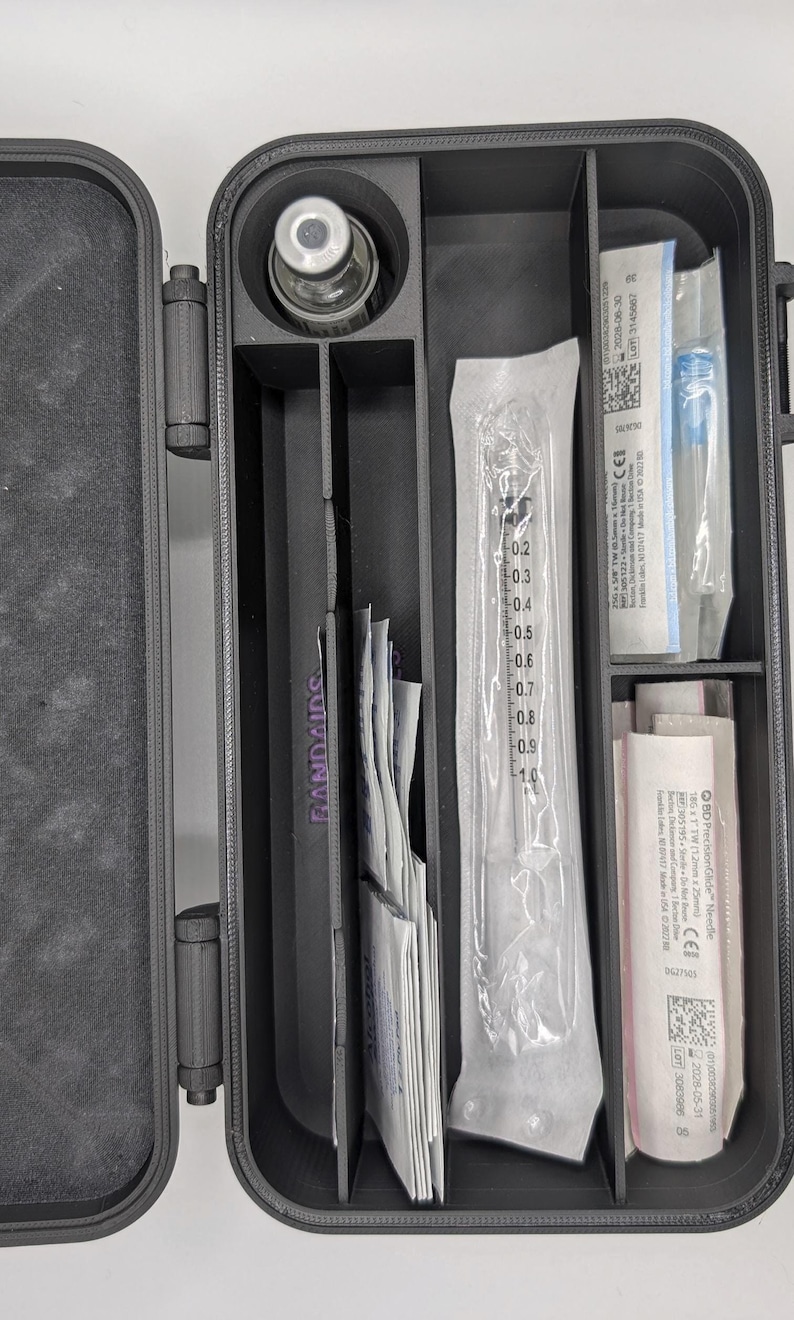 May include: A black, compartmentalized case containing medical supplies. The case holds a vial, syringes, needles, and BAND-AIDS. The case is designed to organize and store medical items. The case is made of a durable material and has a secure closure.