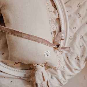 Puede incluir: Un caballo de balanc&iacute;n de tela blanca con una cinta de terciopelo marr&oacute;n y un borde de encaje. El caballo tiene un palo de madera para mango y una peque&ntilde;a etiqueta que dice "boho boho".