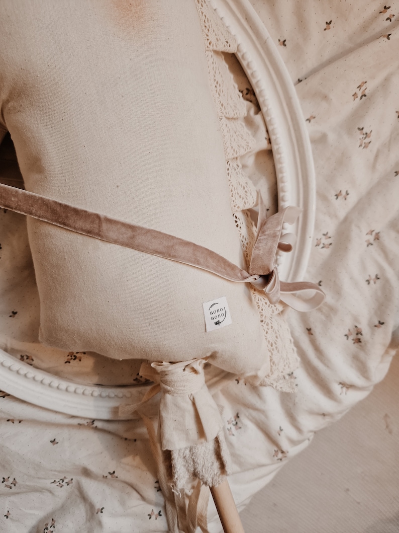 Puede incluir: Un caballo de balanc&iacute;n de tela blanca con una cinta de terciopelo marr&oacute;n y un borde de encaje. El caballo tiene un palo de madera para mango y una peque&ntilde;a etiqueta que dice "boho boho".