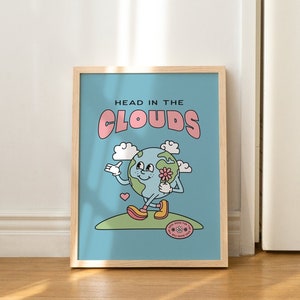 May include: A framed print with a blue background and a cartoon illustration of the Earth holding a flower. The text "HEAD IN THE CLOUDS" is written in pink letters above the Earth.