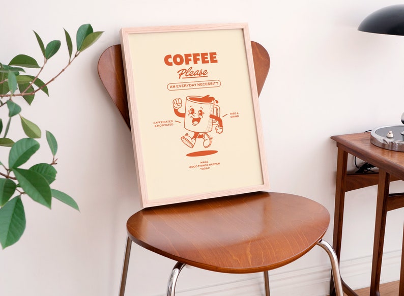May include: A framed print featuring a cartoon coffee cup character. The text reads "Coffee Please, An Everyday Necessity". The coffee cup is smiling and has arms and legs. The text also says "caffeinated & motivated" and "rise & grind".